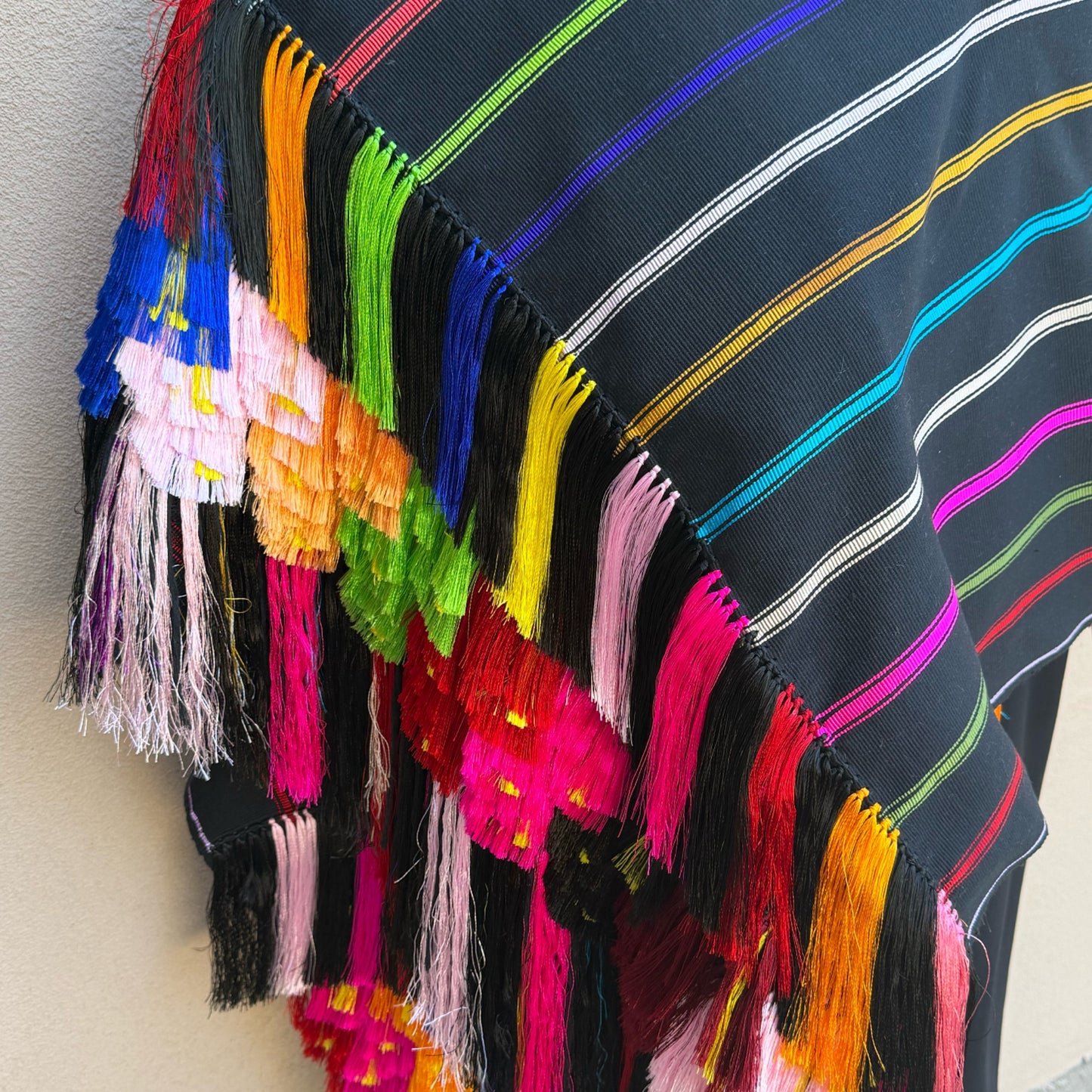 Close-up of hand-knotted silk flower fringe with natural feather accents on a Purepecha backstrap-loom shawl