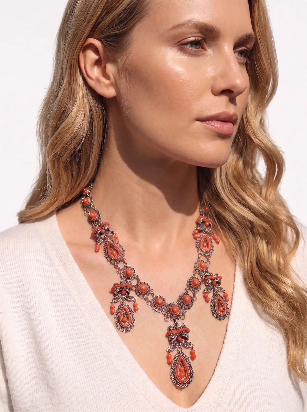 A detailed coral and silver-toned necklace with intricate filigree work, teardrop-shaped beads, and dangling pendants.
