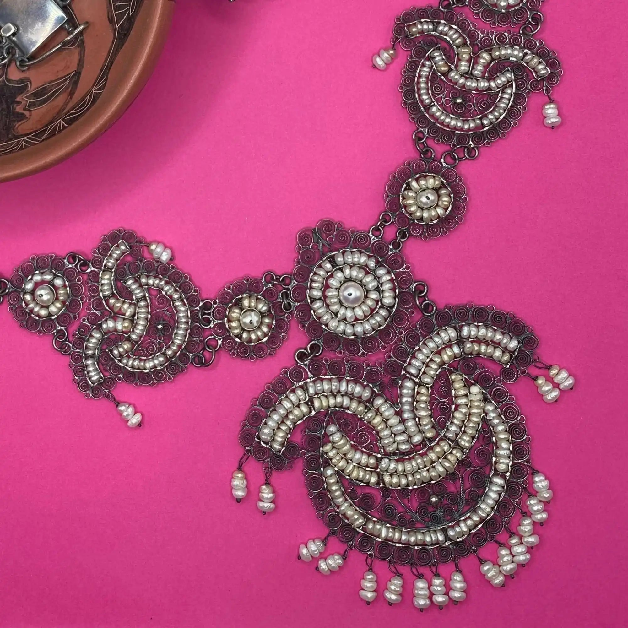 An ornate silver filigree and pearl necklace.
