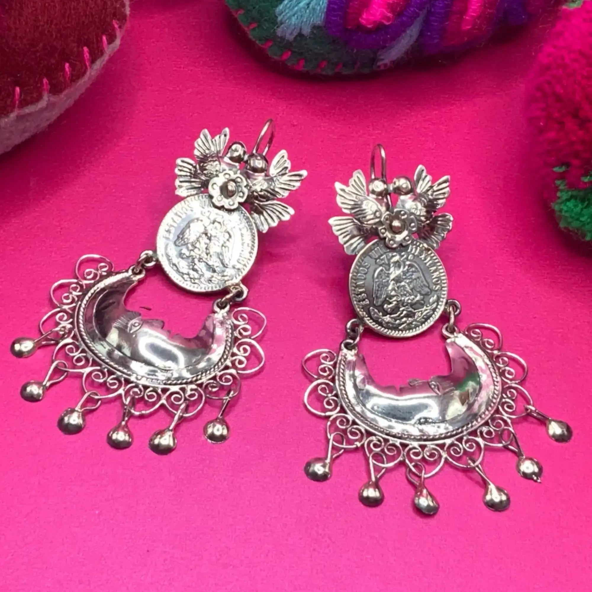 Silver coin earrings with intricate floral and crescent moon designs, featuring dangling bells.