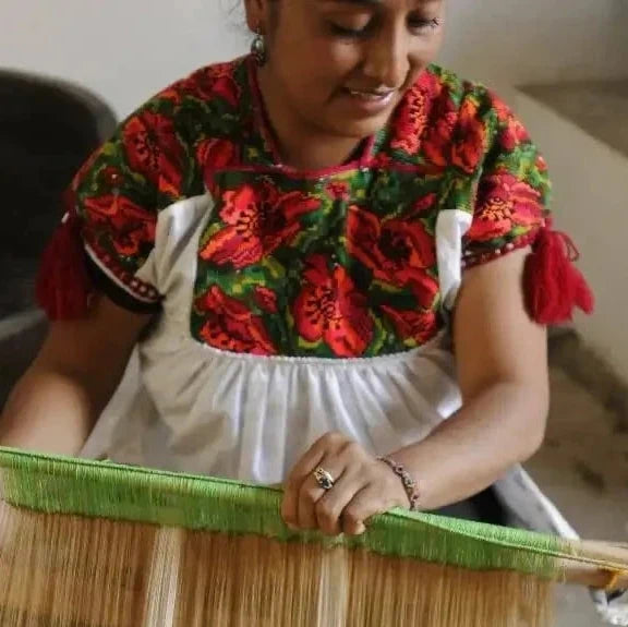 A traditional wooden loom with natural-colored threads and a vibrant green warp thread.