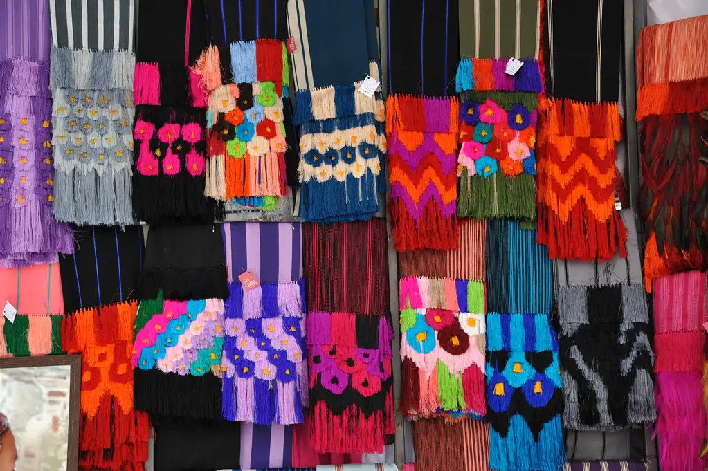 Vibrant, handwoven textile scarves with bold geometric and floral patterns in multicolored yarns.