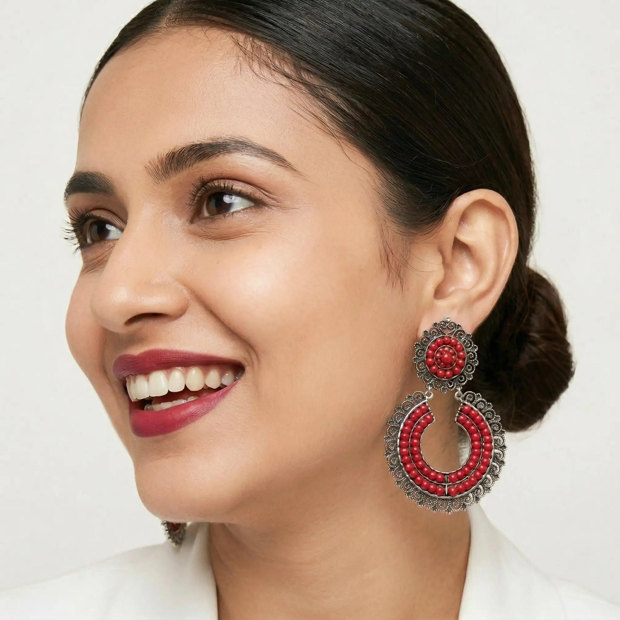 Vibrant red beaded chandelier earrings with intricate silver-toned metalwork and a circular design.